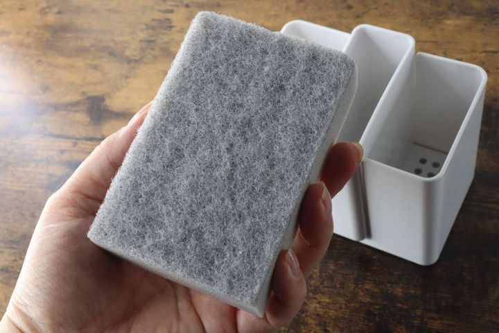 手がグレーの付属スポンジを掴んでおり、背景に白い収納ケースが写っている