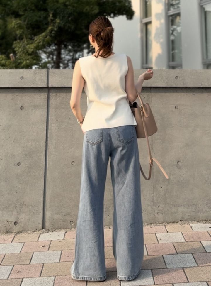 白いノースリーブとカーブデニムを着用し後ろ姿を見せる女性