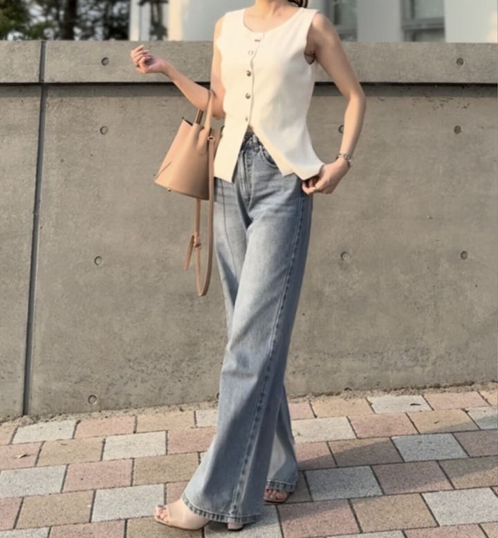 白いノースリーブとカーブデニムを着用し歩く女性