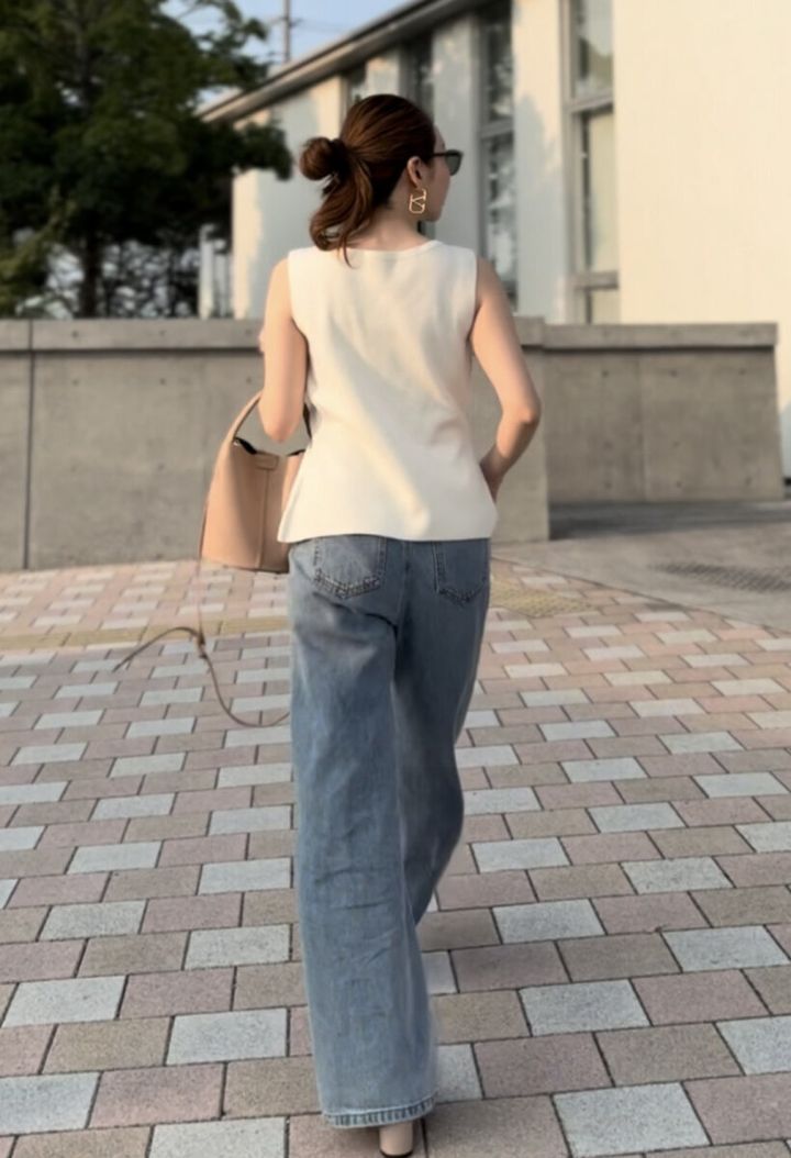 白いノースリーブとカーブデニムを着用し歩く女性の後ろ姿
