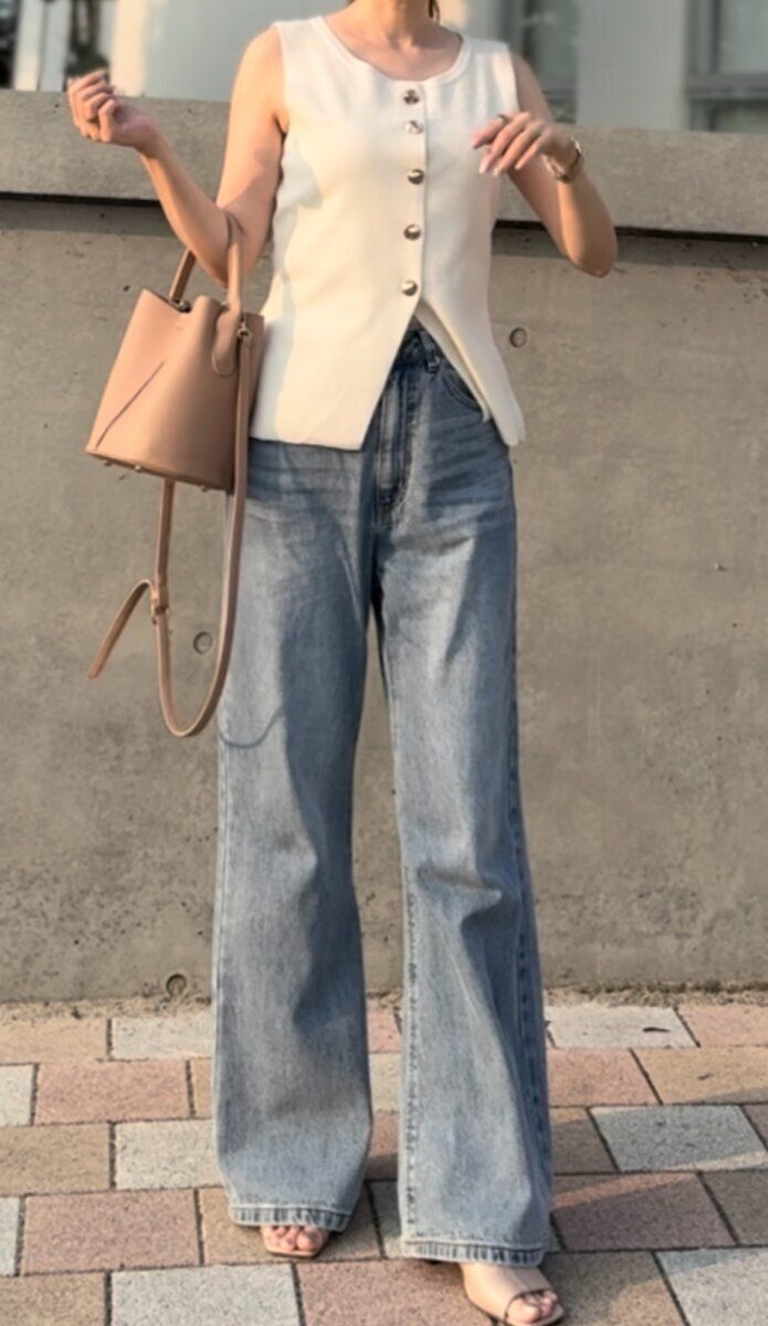 白いノースリーブとカーブデニムを着用し立つ女性