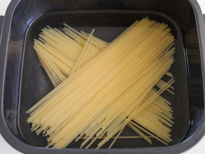 黒い耐熱容器に半分に折ったスパゲッティと水が入っている様子