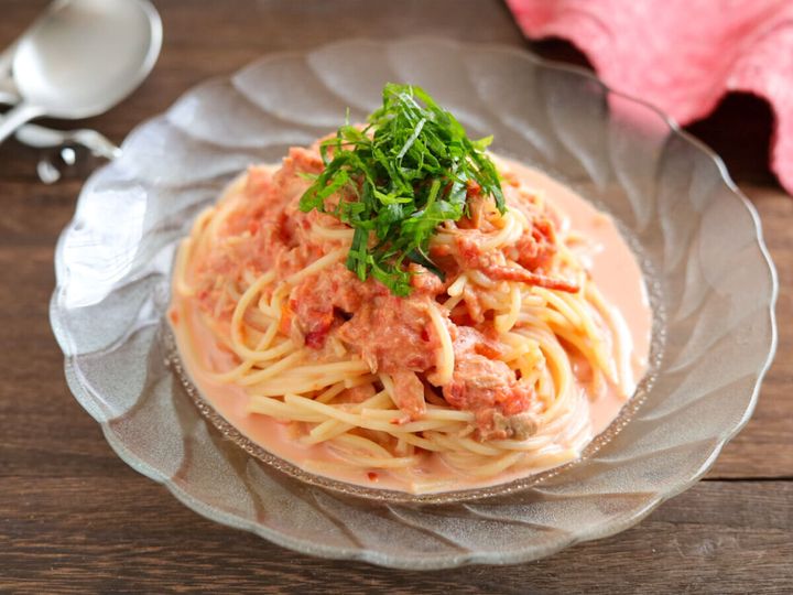ガラスの器に盛り付けられた冷製パスタに青じそがトッピングされ、奥にスプーンと布巾が見える食卓の様子