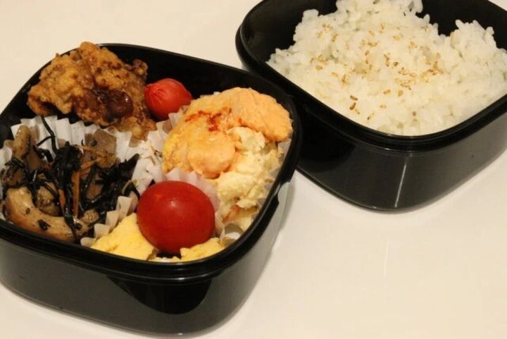 黒い二段弁当箱におかずとご飯が美味しそうに詰められている