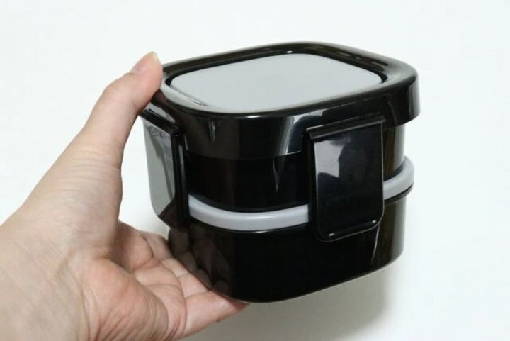 手で持たれた黒い二段弁当箱。ロック蓋が閉じた状態