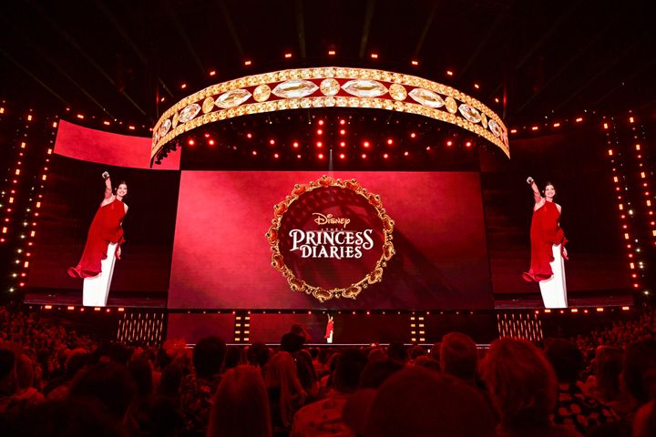 Disney Entertainment Showcaseのステージで観客に手を振るアン・ハサウェイ