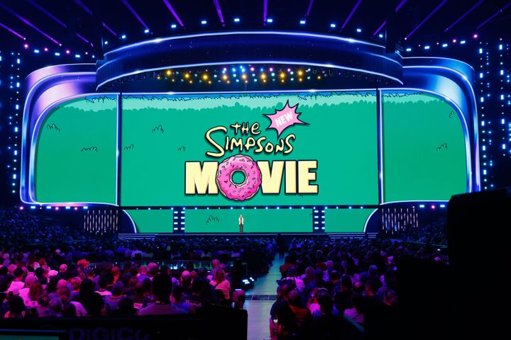 THE NEW SIMPSONS MOVIEのロゴが映し出されたステージに立つデイナ・ウォルデン