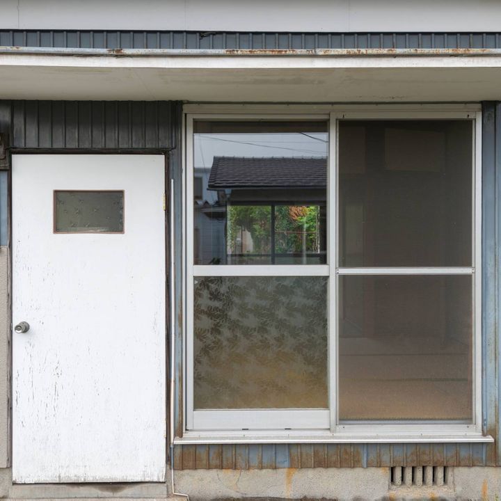 古い空き家。大きい扉の横に窓がある外観
