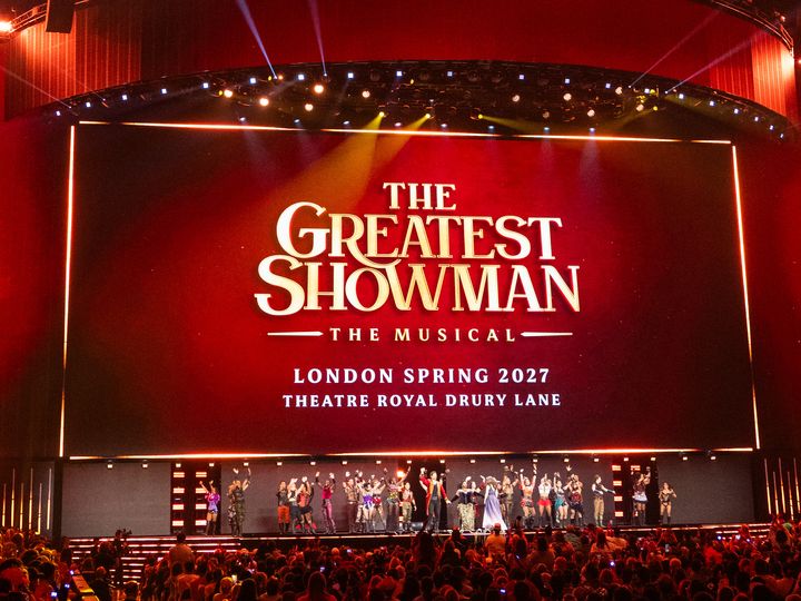 手を挙げて客席の歓声に応えるThe Greatest Showmanのカンパニー