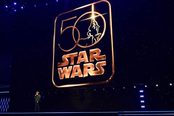 スター・ウォーズ50周年のロゴが浮かぶステージに立つデイヴ・フィローニ