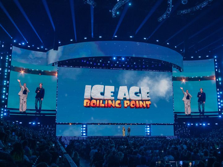 ICE AGE BOILING POINTのロゴを背に手を挙げるクイーン・ラティファとデニス・レアリー