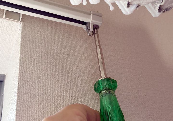 緑色のドライバーを使ってカーテンレールのキャップストップを外している手元