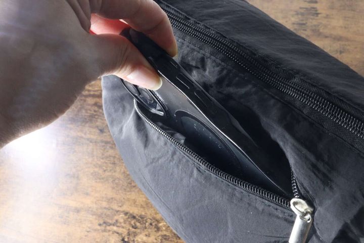 黒いバッグのフロントポケットにスマートフォンを入れる手元