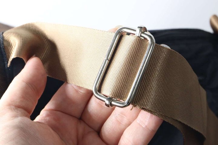 ベージュの太いストラップと金属製の金具を指でつまんで素材感を示す