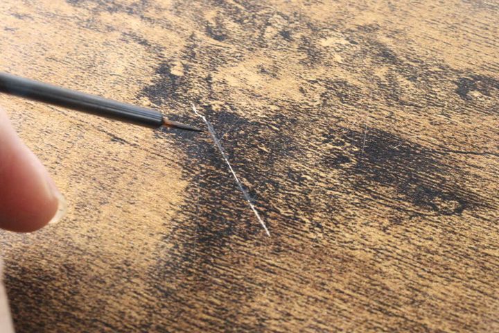 木目調の机の白い傷に筆で絵の具を塗る様子