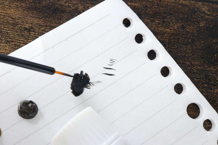 白い紙に出した黒い絵の具を筆で混ぜている