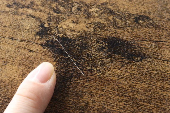 木目調の机の天板にある白い傷を指で示す