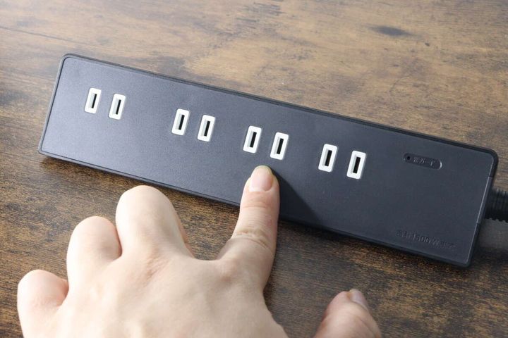 黒いテーブルタップの差し込み口を指で押している