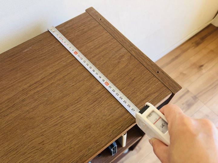 女性がメジャーで木製棚の奥行きを測る様子