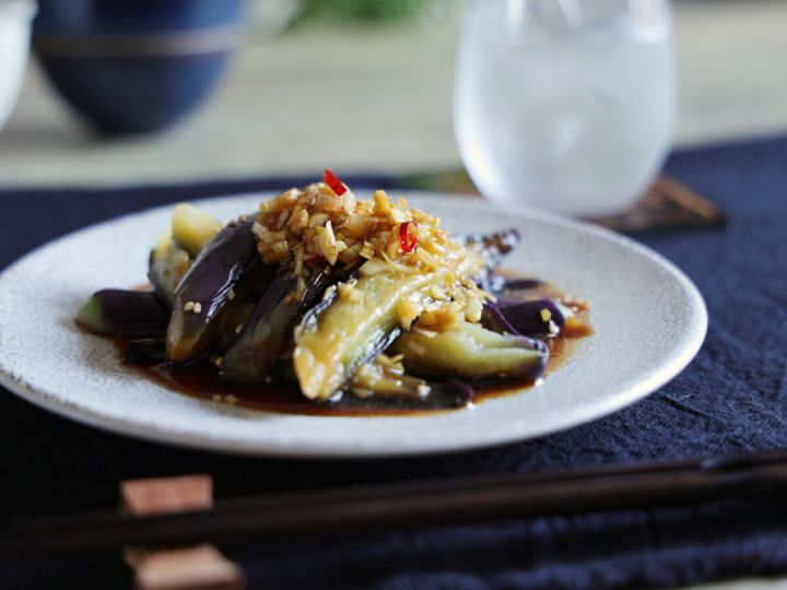 白い皿に盛り付けられたごま香る中華風蒸しなす、奥にグラス