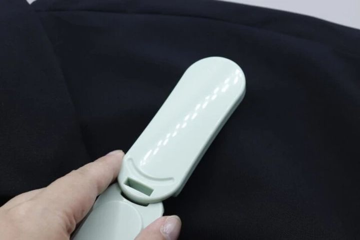黒い服の表面を薄緑色の洋服ブラシでブラッシングしている様子