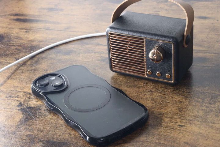 スマートフォンと黒いレトロスピーカーが木目のテーブルに並べられている。