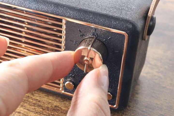 指でレトロスピーカーのゴールドのダイヤルを回そうとしている様子。
