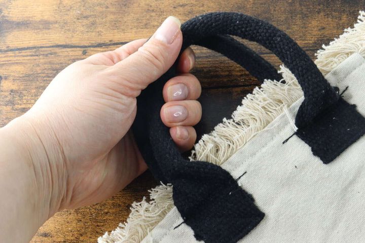 女性の手がフリンジトートバッグの黒い持ち手を握っている。持ち手の太さがわかる