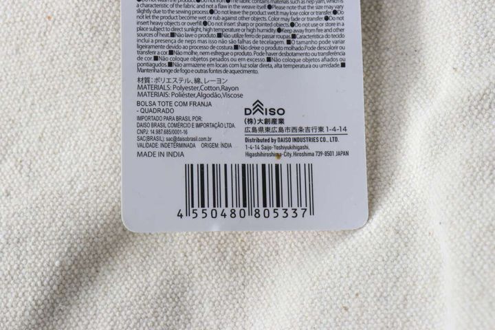 フリンジトートバッグの商品タグ裏面。バーコードと商品情報、素材、製造元が記載されている