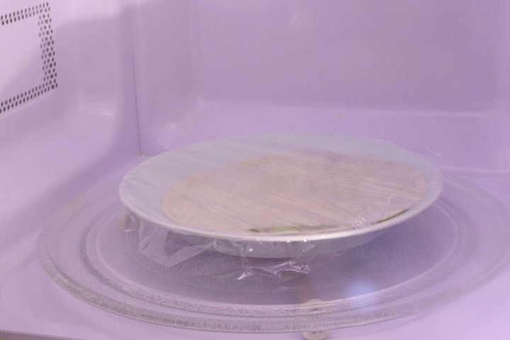電子レンジの中でラップをかけて温められているトルティーヤ