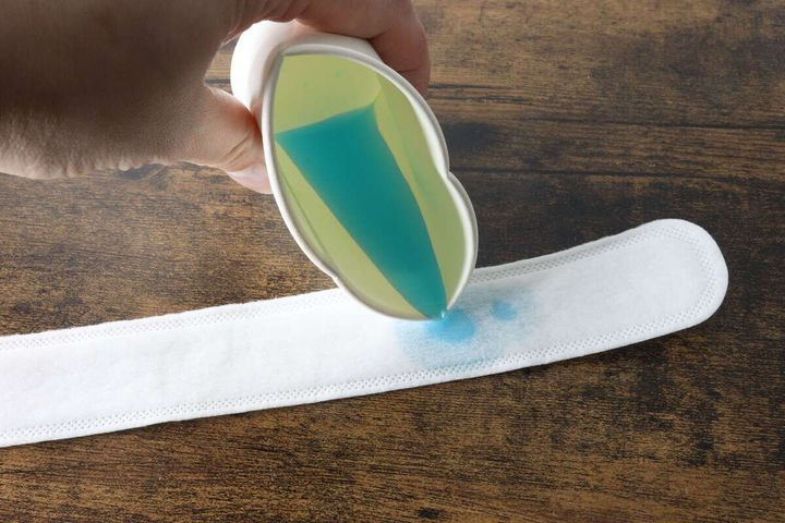 青い液体を計量カップから白い汗取りパットに注いでいる