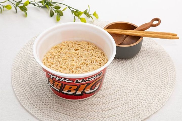 ブタメン超BIGの麺が見えるカップ麺が白い敷物の上に置かれている
