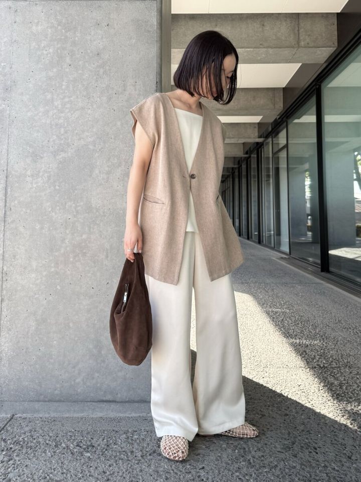 ベージュのジレと白いワイドパンツを着用し、茶色いバッグを持つ女性