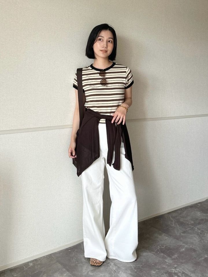 ボーダーTシャツと白いワイドパンツを着用し、腰に茶色いカーディガンを巻いた女性