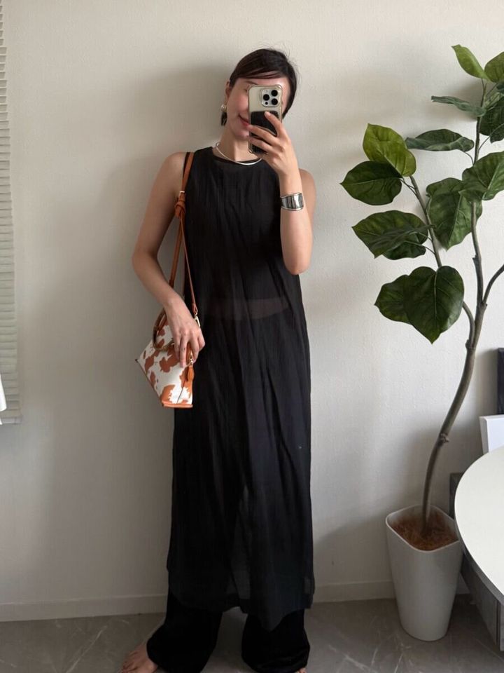 サテンパンツに黒いシアーワンピースをレイヤードしたコーデで自撮りする女性