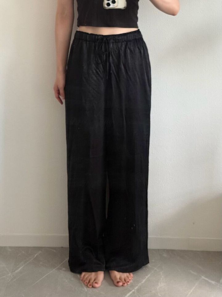 黒いサテンイージーパンツを着用し正面を向く女性