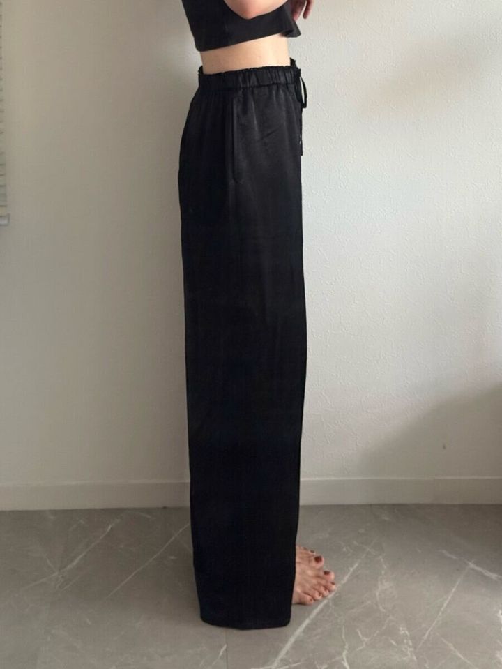 黒いサテンイージーパンツを着用し横向きに立つ女性