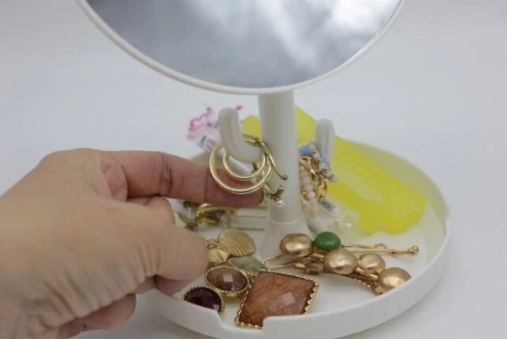 白いスタンドミラーのトレーにアクセサリーを置き指で触っている