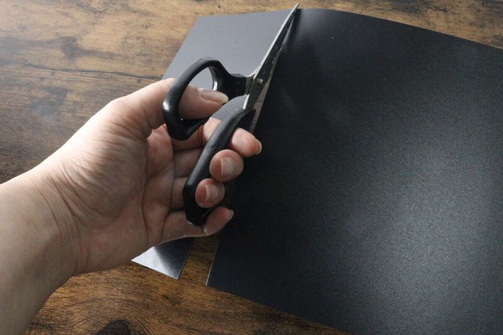 女性の手がハサミで黒いプラ底板をカットしている様子
