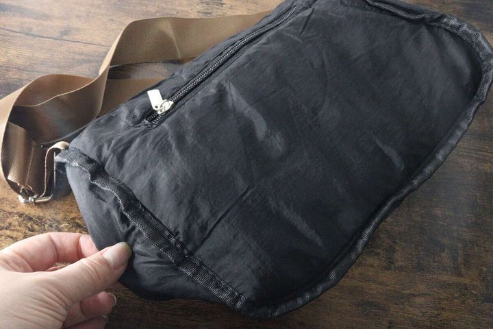 女性の手がくたっとした黒いショルダーバッグの底を触っている