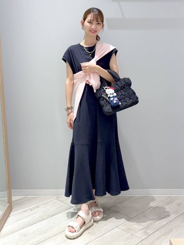 黒いノースリーブワンピースにピンクカーデを肩掛けした女性