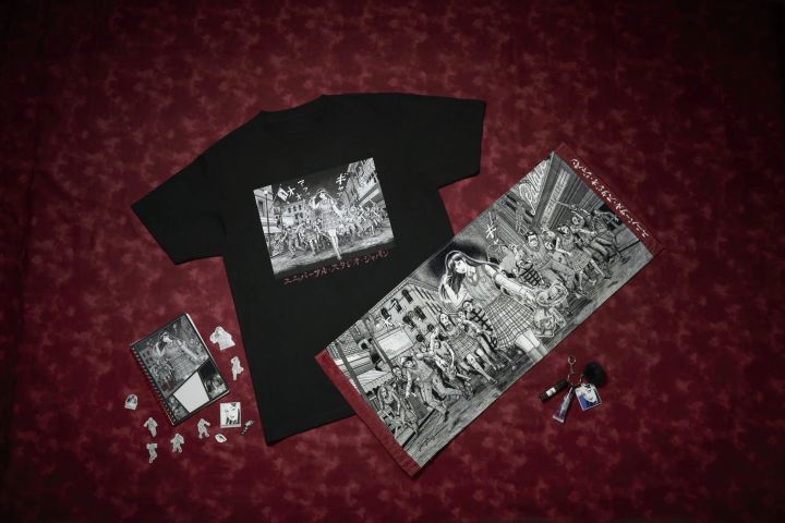 伊藤潤二氏描きおろしアートを使用した黒いTシャツとフェイスタオル、ステッカー付きノート、チャーム付きコスメキーチェーンを並べた富江×ストリート・ゾンビのコラボグッズ