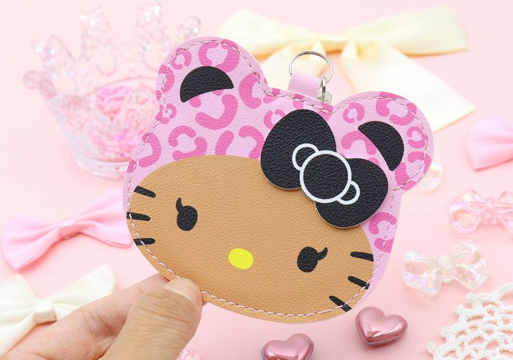 女性の指がヒョウ柄キティのミラーチャームを持つ。背景に装飾品