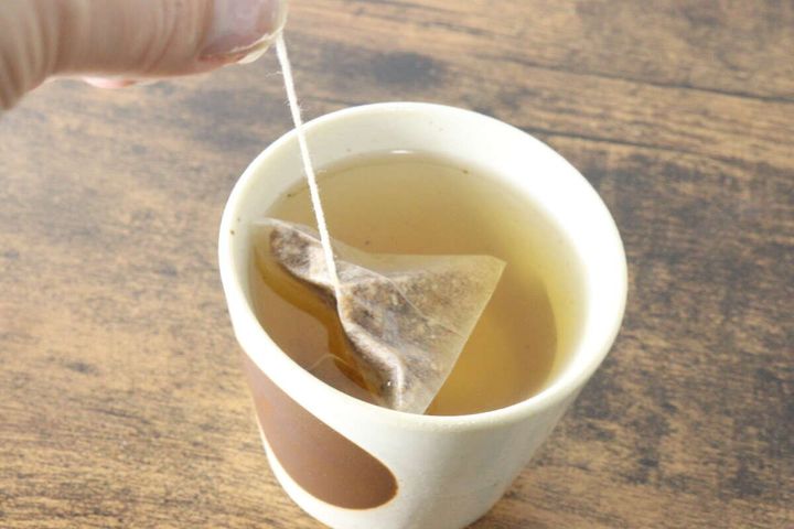 茶碗に入ったごぼう茶のティーバッグを指で持ち上げている様子