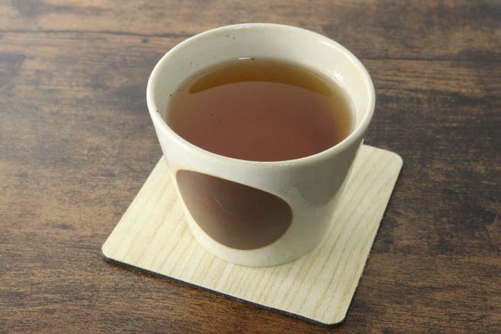 茶碗に入った琥珀色の温かいごぼう茶がコースターの上に置かれている