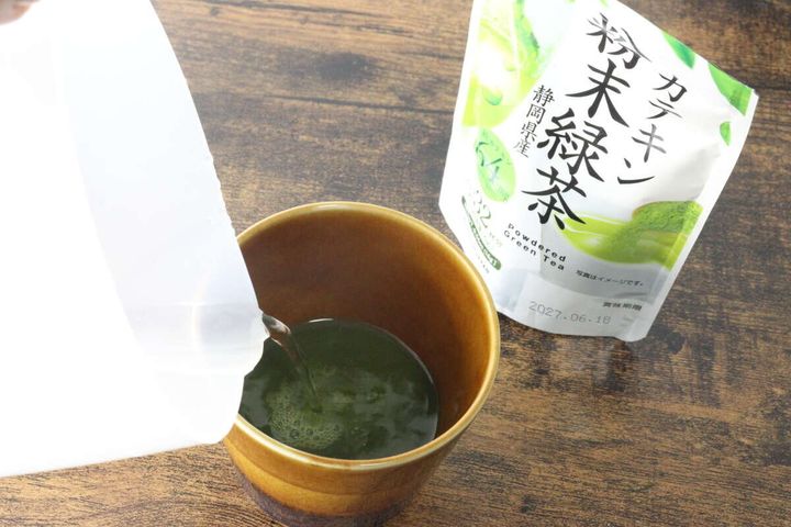 茶碗に入った緑茶の粉末に、白い容器からお湯を注いでいる様子