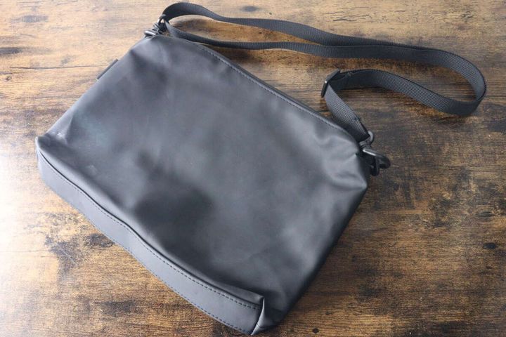 黒いショルダーポーチが木製テーブルに斜めに置かれている