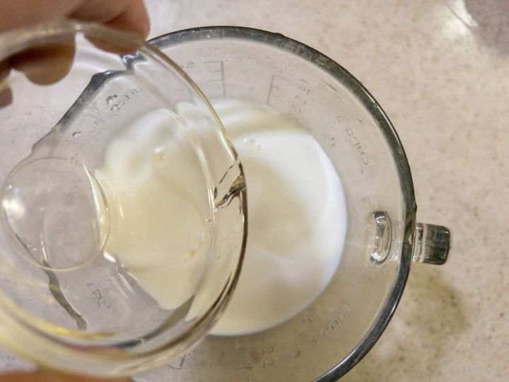 計量カップに入った牛乳に、別の計量カップから溶かしたゼラチン液を注ぎ入れている手元のアップ