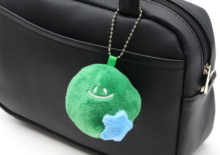 緑色の丸いぬいぐるみキーホルダーが黒いバッグに付けられている様子
