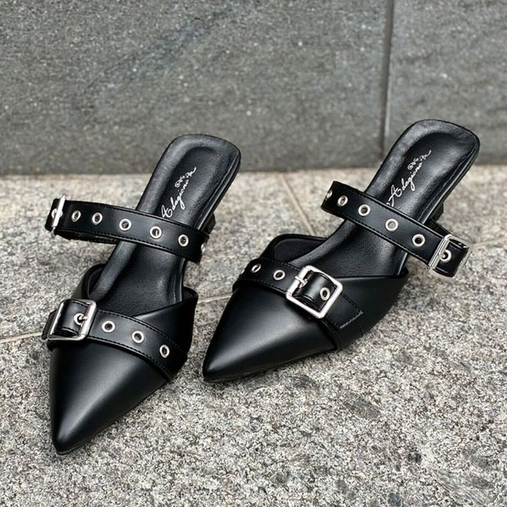 黒いポインテッドトゥのダブルベルトミュールパンプスが屋外に置かれている